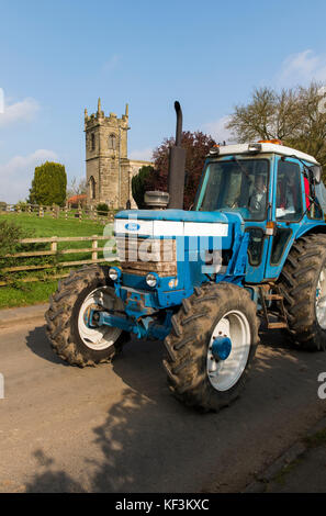 Man driving blue vintage tractor in parade through Bugthorpe village for annual charity event - Wolds Vintage Group Road Run, Yorkshire, England, UK. Stock Photo