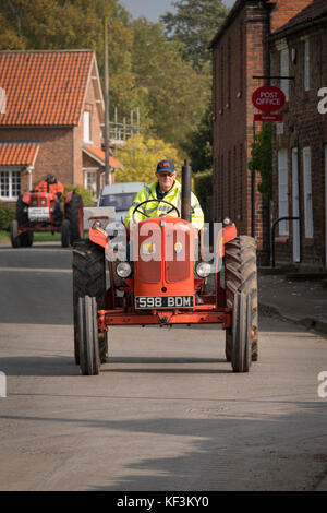 Man driving red vintage BMC tractor through village of Bugthorpe on Wolds Vintage Group Road Run, an annual charity event - Yorkshire, England, UK. Stock Photo