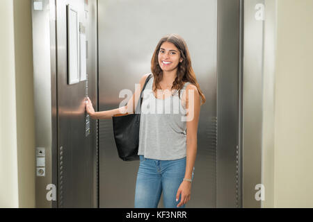 Smiling Young Woman Standing In Elevator And Pressing Button Stock Photo