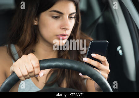 Young Woman Looking At Her Mobile Phone While Sitting Inside Car Stock Photo