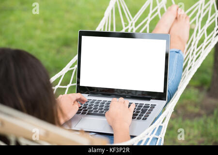 Smiling Young Woman Lying On Hammock Using Laptop Stock Photo