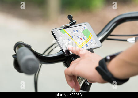 Close-up Of Human Hand Pointing At Smart Phone Showing GPS Navigation On Bicycle Stock Photo