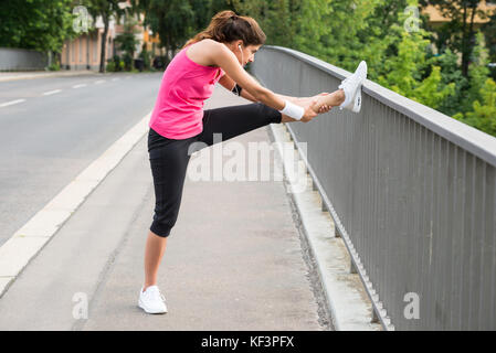 Young Woman Stretching Her Legs Over Fence At Road Stock Photo