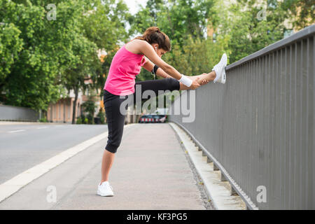 Young Woman Stretching Her Legs Over Fence At Road Stock Photo