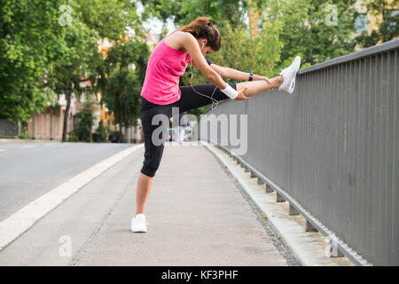 Young Woman Stretching Her Legs Over Fence At Road Stock Photo