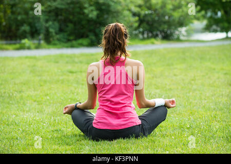 Young Woman Sitting On Grass Meditating In Park Stock Photo