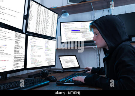 Boy Programming On Computer With Multiple Monitors And Laptop On Desk Stock Photo