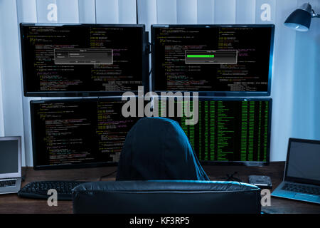 Rear View Of A Boy Sitting On Chair Hacking Multiple Computers Stock Photo