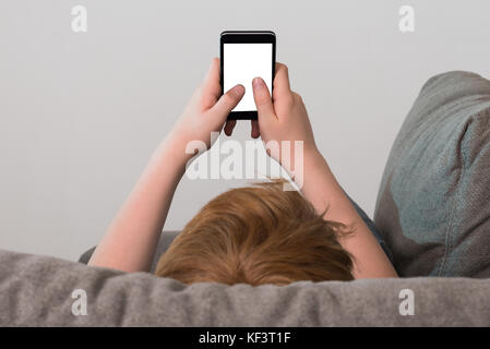Boy Lying On Sofa Holding Cellphone With Blank Screen Stock Photo