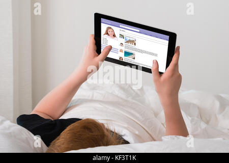 Boy Lying On Bed Chatting On Social Networking Site Using Digital Tablet At Home Stock Photo