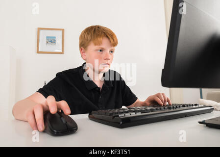 Boy Sitting On Chair Using Computer At Home Stock Photo
