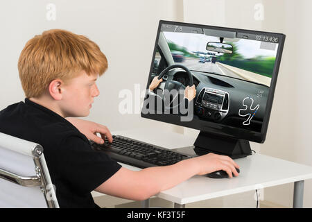 Boy Sitting On Chair Playing Car Game On Computer At Home Stock Photo