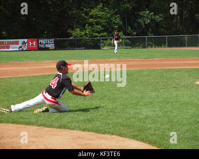 Youth baseball player attempting to field a baseball and ultimately falls. Stock Photo