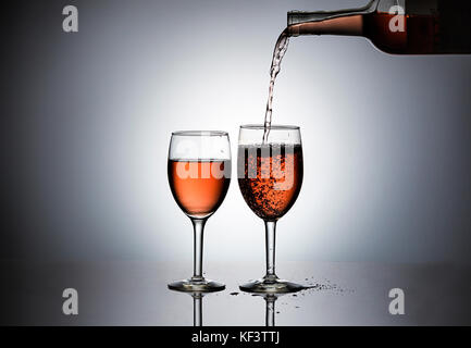 Pouring rose' wine form a bottle into wine glasses. Stock Photo