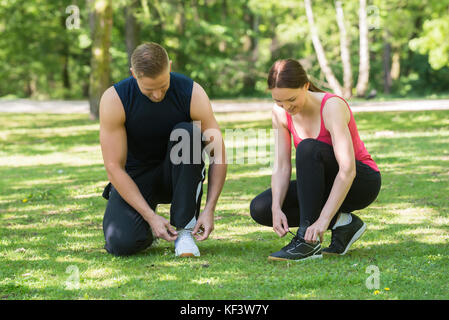 Young Happy Couple Tying Shoes In Park Stock Photo