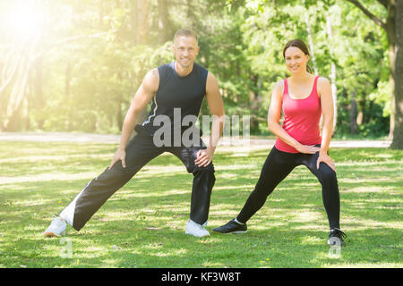 Young Happy Athletic Couple Doing Exercise In Park Stock Photo