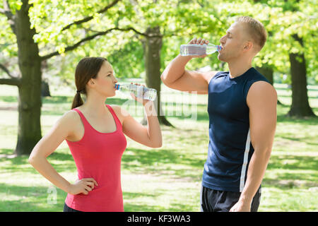Young Athletic Couple Drinking Water After Exercise In Park Stock Photo