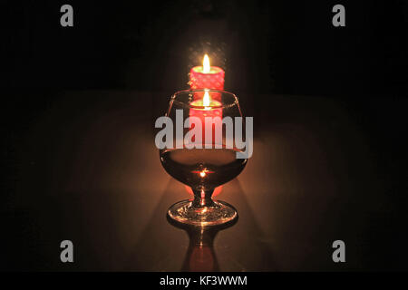 A glass of cognac or whiskey and candle on black background. christmas composition. Stock Photo