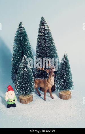 Vintage photography filtered of Staging of full artificial firs like a small snowy forest tree with a figurine reindeer inside and a garden gnome besi Stock Photo
