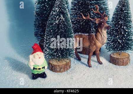Vintage photography filtered of Staging of full artificial firs like a small snowy forest tree with a figurine reindeer inside and a garden gnome besi Stock Photo