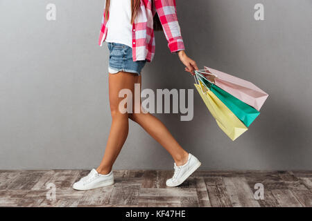 Cropped photo of young woman in casual wear holding shopping bags, over gray background Stock Photo