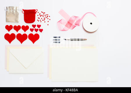 Display of love letter items on white background. Assortment of cards, envelopes, hearts, ribbon and ink pen. Stock Photo