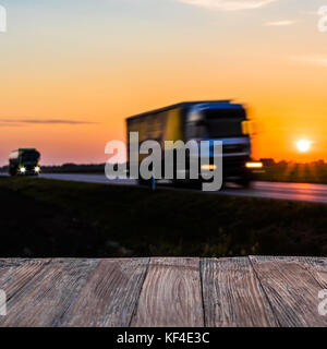 Two Trucks Driving on Highway at Vibrant Sunset with Wooden Foreground Stock Photo