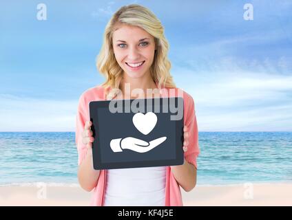 Digital composite of Woman holding tablet with hand giving heart icon Stock Photo