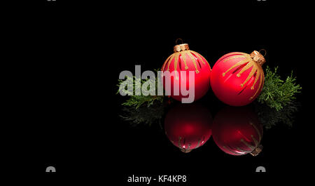 Christmas card template in luxury style, premium. Two red Christmas balls decorations with branches of an evergreen tree isolated on a black glossy ba Stock Photo
