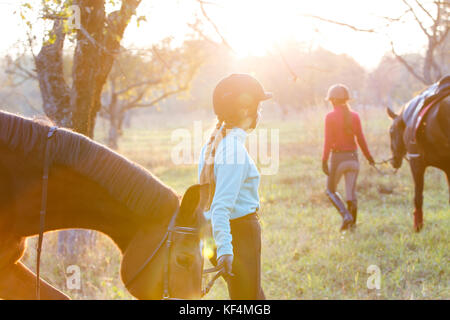 Group of rider girls walking with horses in park. Equestrian recreation activities background with copy space Stock Photo