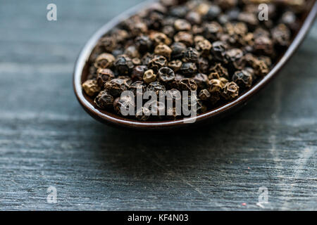 Studio shot of spoon filled with black dried pepper seeds on dark background Stock Photo