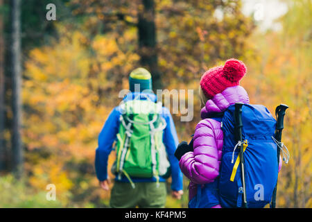 Happy couple hikers trekking in beautiful yellow autumn forest and mountains. Young people man and woman walking on trek trail with backpacks, healthy Stock Photo