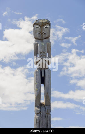 Maori traditional carved wooden pou or guardian outside a marae in New Zealand Stock Photo