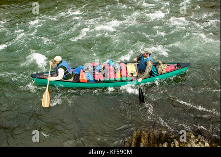 Two men navigate an overloaded canoe through rushing rapids during an adventure on a wild Alaskan river. Stock Photo