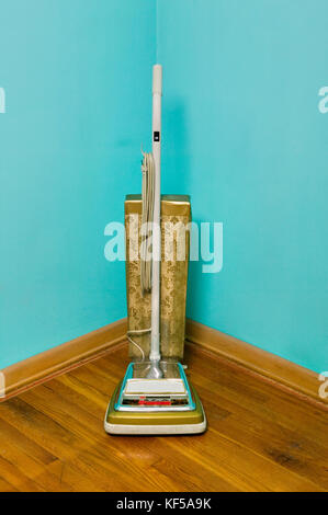 Vintage vacuum cleaner standing in room corner against turquoise walls Stock Photo