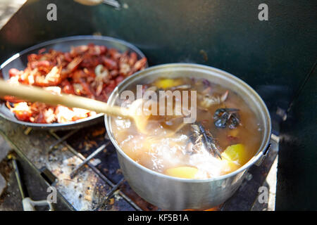 Cooking fresh fish and crawdads over a dirty portable camping gas burner in a boiling pot and pan in a close up view Stock Photo