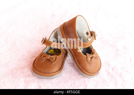 Pair of brown Mary Jane style baby shoes against a pale pink background. Stock Photo