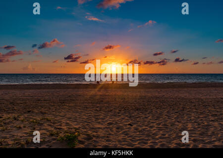 silhouettes of people walking through early morning light rays from the sun shining on a sandy beach Stock Photo