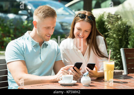 Young Happy Couple Sitting On Bench Using Mobile Phone Stock Photo