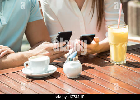 Close-up Of Young Happy Couple Sitting On Bench Using Mobile Phone Stock Photo