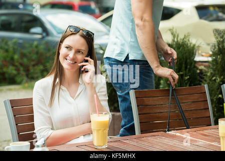 Male Thief Stealing Purse Of A Young Woman Using Mobile Phone Stock Photo