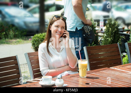 Male Thief Stealing Purse Of A Young Woman Using Mobile Phone Stock Photo