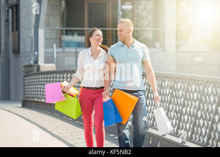 Young Happy Couple Walking On Bridge With Multi-colored Shopping Bags Stock Photo