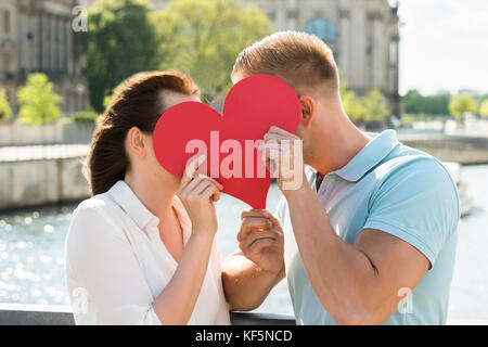Close-up Of Young Couple Hiding Behind Heart Shape Stock Photo