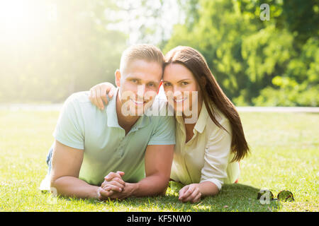 Happy Young Couple Lying On Green Grass At Park Stock Photo