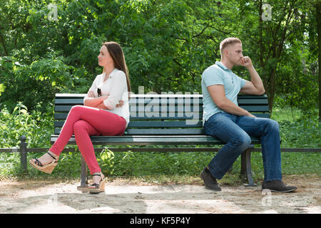 Displeased Young Couple Sitting On Bench In Park Stock Photo