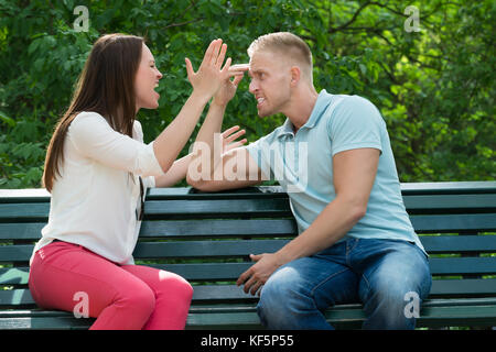 Young Couple Sitting On Bench Quarreling With Each Other At Park Stock Photo