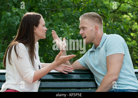 Young Couple Sitting On Bench Quarreling With Each Other At Park Stock Photo