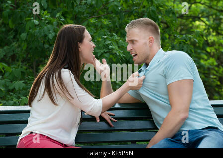 Young Couple Sitting On Bench Quarreling With Each Other At Park Stock Photo