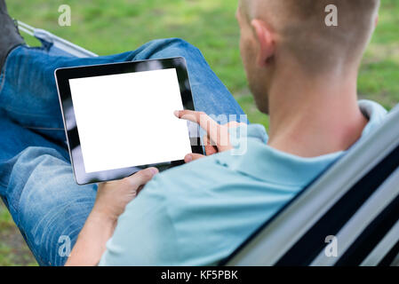 Young Man Using Digital Tablet While Lying In Hammock Stock Photo